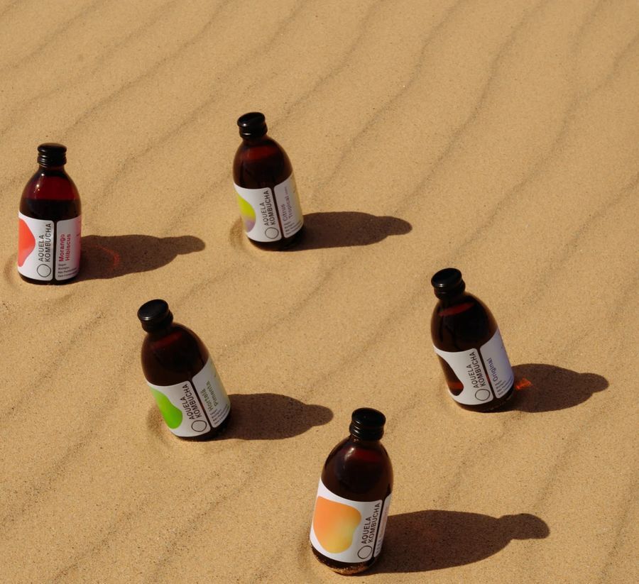 Cinco garrafas Aquela Kombucha espetadas numa duna