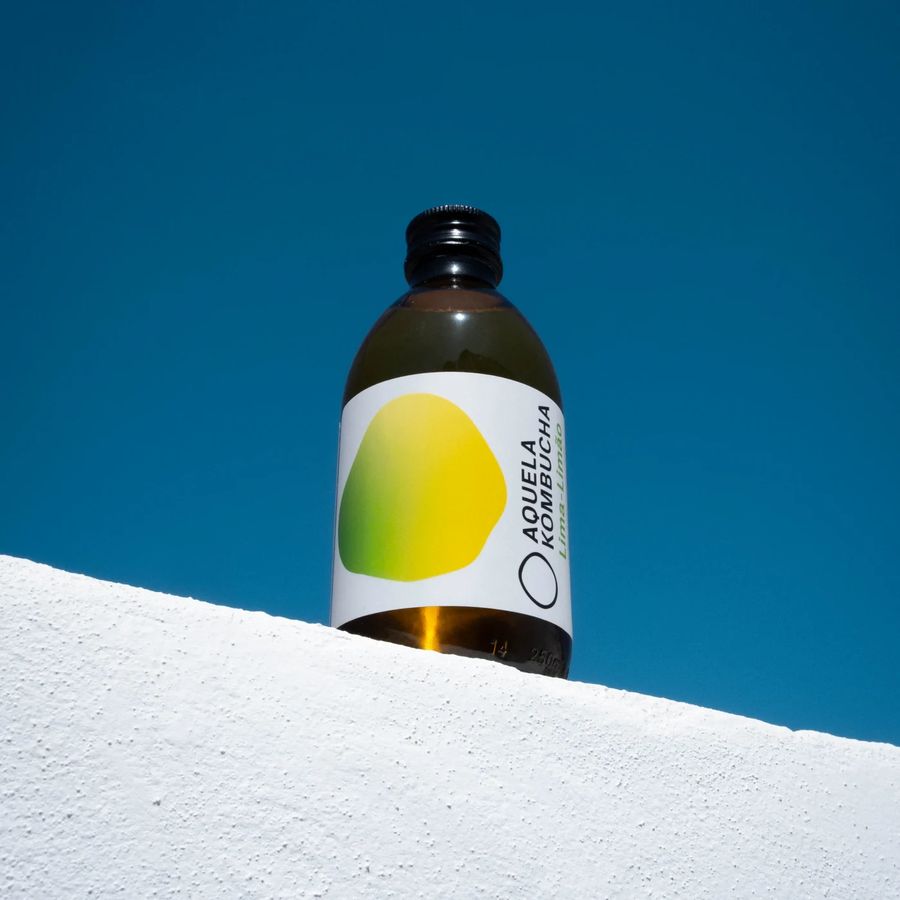 Garrafa Aquela Kombucha Lima-Limão sobre muro branco e céu azul